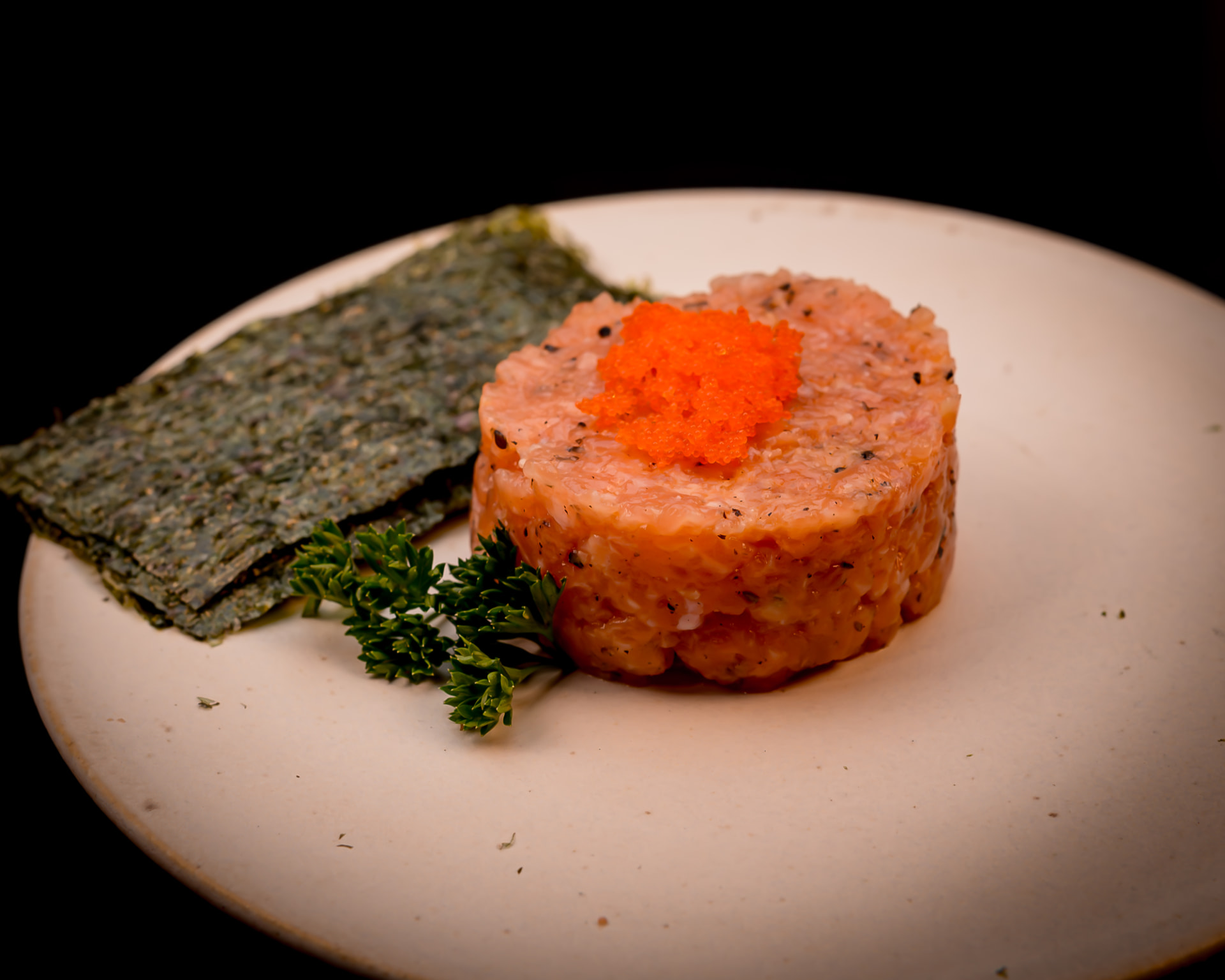 Tartar de salmão moldado em disco, com ovas laranjas, folhas de alga e ervas